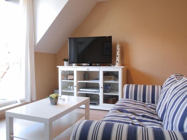 A living room with a white TV stand, a striped sofa, and a small table with a plant. - Cezanne (Nieuwpoort)