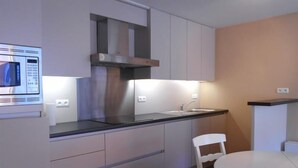 A modern kitchen with white cabinets, a stainless steel range hood, a black countertop, a white sink, and a small dining table with two chairs. - Cezanne (Nieuwpoort)