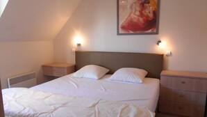 A bedroom with a large bed, two bedside tables, a nightstand, a radiator, and a painting on the wall. - Cezanne (Nieuwpoort)