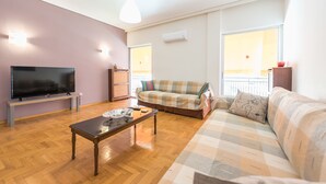 A living room with a flat-screen TV, a wooden coffee table, a sofa, and a window with a view. - Comfortable Apartment near City Center (Athens)