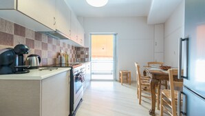 A modern kitchen with a built-in oven, a coffee maker, and a dining area with wooden chairs and a table. - Comfortable Apartment near City Center (Athens)
