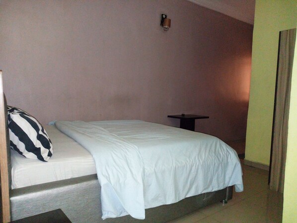 Une petite chambre avec un lit simple, un mur uni, une table de chevet et un oreiller.
