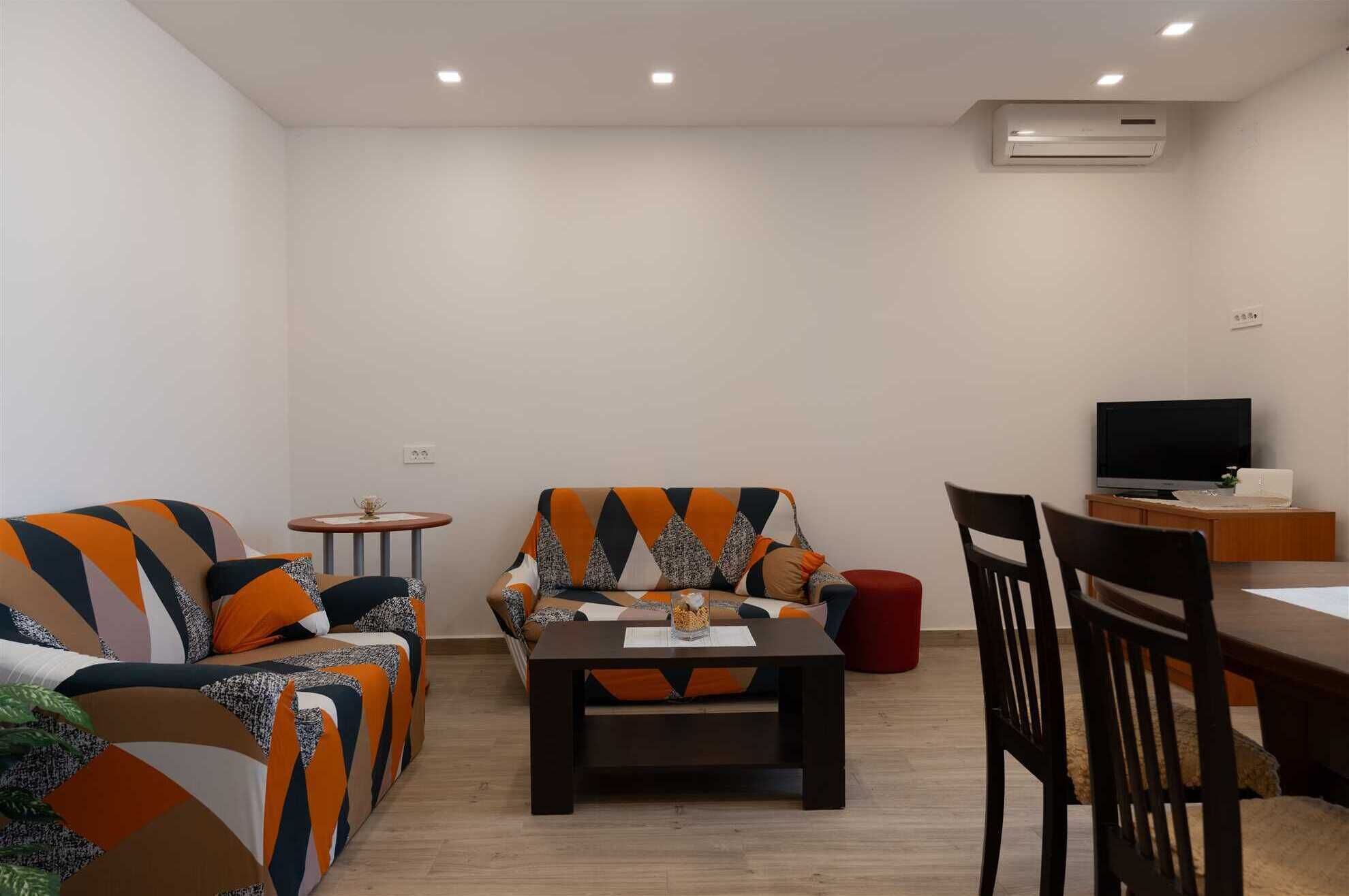 A living room with a sofa, a coffee table, a TV, and a dining area.