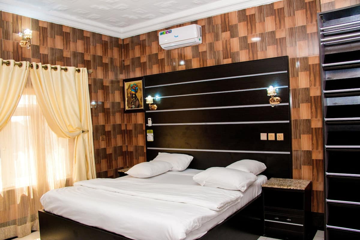 A modern hotel room with a wooden wall panel design, a large bed with white linens, a bedside table, and a built-in wardrobe.