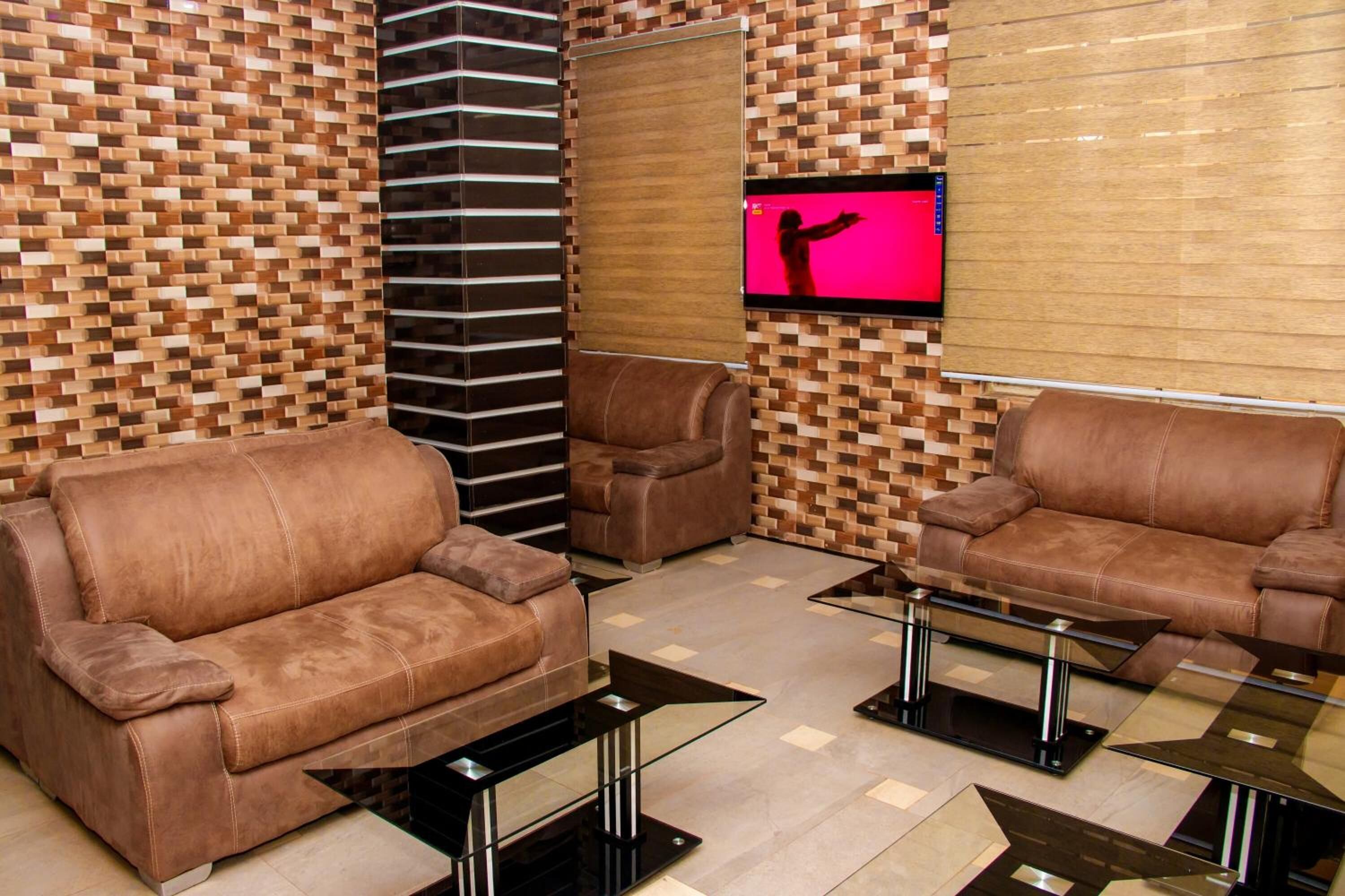 Een moderne woonkamer met twee bruine leren banken, een glazen salontafel en een aan een houten muur bevestigde televisie.