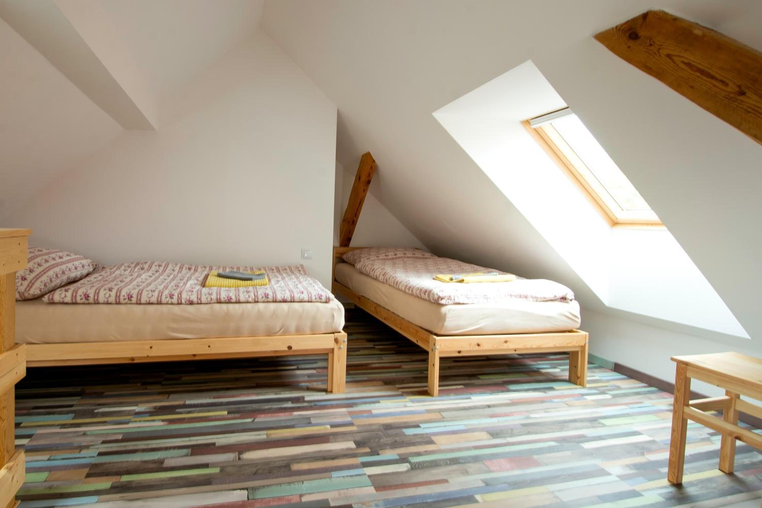 Un dormitorio con dos camas de madera, techo inclinado, tragaluz y suelo de madera multicolores.