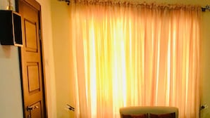 A room with a sofa, a door, a wall-mounted speaker, and a curtain.