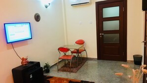 A room with a television, a small table with two chairs, a door, and a wall-mounted air conditioner.