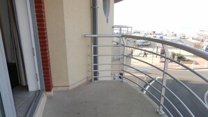 A balcony with a metal railing, a concrete floor, and a view of a parking area with cars and a building in the background. - Zeezicht 201 (Nieuwpoort)