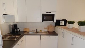 A compact kitchen with white cabinets, a black microwave, a coffee maker, and a wooden cutting board. - Zeezicht 201 (Nieuwpoort)