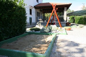 Enjoy a serene garden retreat with a sandpit and patio area surrounded by lush plants and a Mediterranean-inspired design.