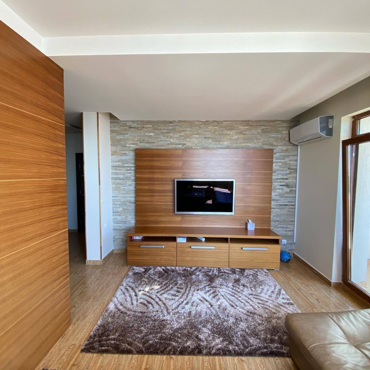 Un salon moderne avec un téléviseur à écran plat fixé à un meuble mural en bois, un tapis à motifs et un canapé en cuir.
