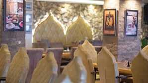 A restaurant interior with cushioned chairs, a stone wall, and framed pictures on the walls.