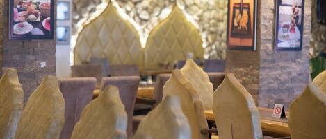 A restaurant interior with cushioned chairs, a stone wall, and framed pictures on the walls.