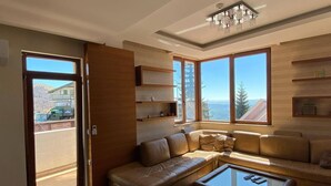 A modern living room with a leather sofa, a glass coffee table, and a large window offering a view of the outdoors.
