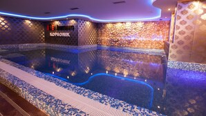 A modern indoor swimming pool with a stone wall and mosaic tiles.