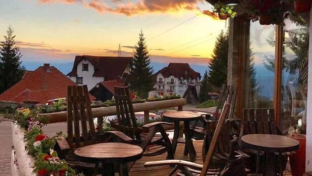 An outdoor seating area with wooden tables and chairs, overlooking a town with traditional buildings.