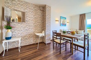 Una habitación con pared de piedra, una mesa de comedor con sillas, una silla blanca, una mesita con un jarrón y un cuadro en la pared.