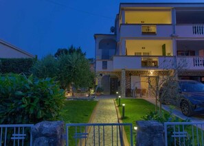 Un edificio residencial de varios pisos con fachada de piedra, un camino de entrada pavimentado y un acceso con portón.