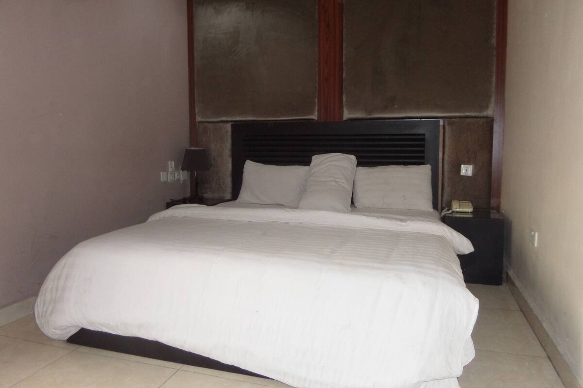 A neatly made bed with a dark headboard and two bedside tables, one with a lamp.