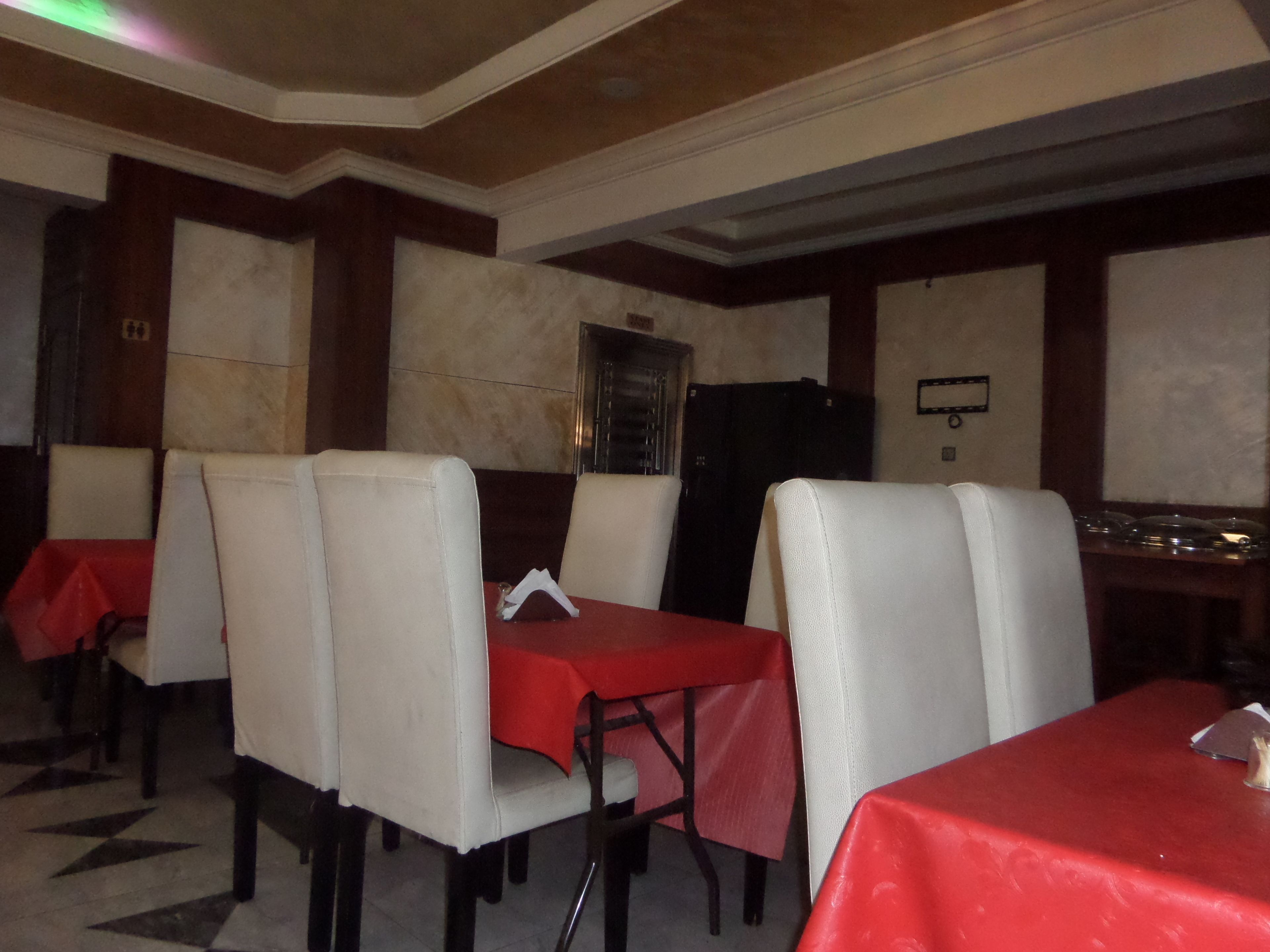 Ein Restaurant mit weißen gepolsterten Sitzecken, roten Tischdecken und einem gefliesten Boden.