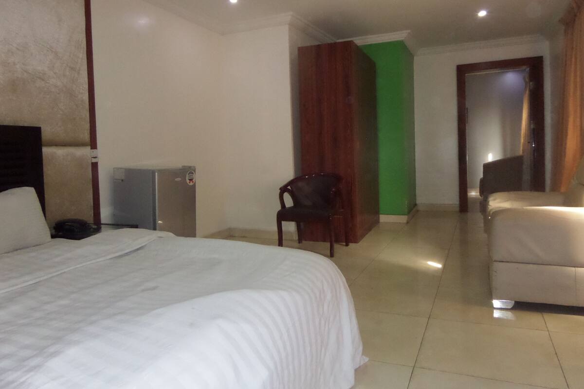 A hotel room with a bed, a chair, a desk, and a green accent wall.