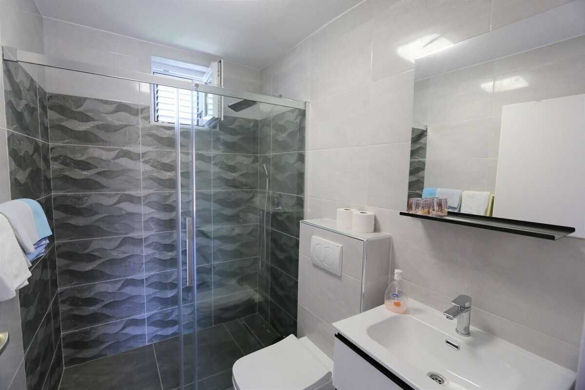 Une salle de bain avec une douche à parois de verre, des toilettes blanches, un lavabo avec un miroir et un porte-serviettes.