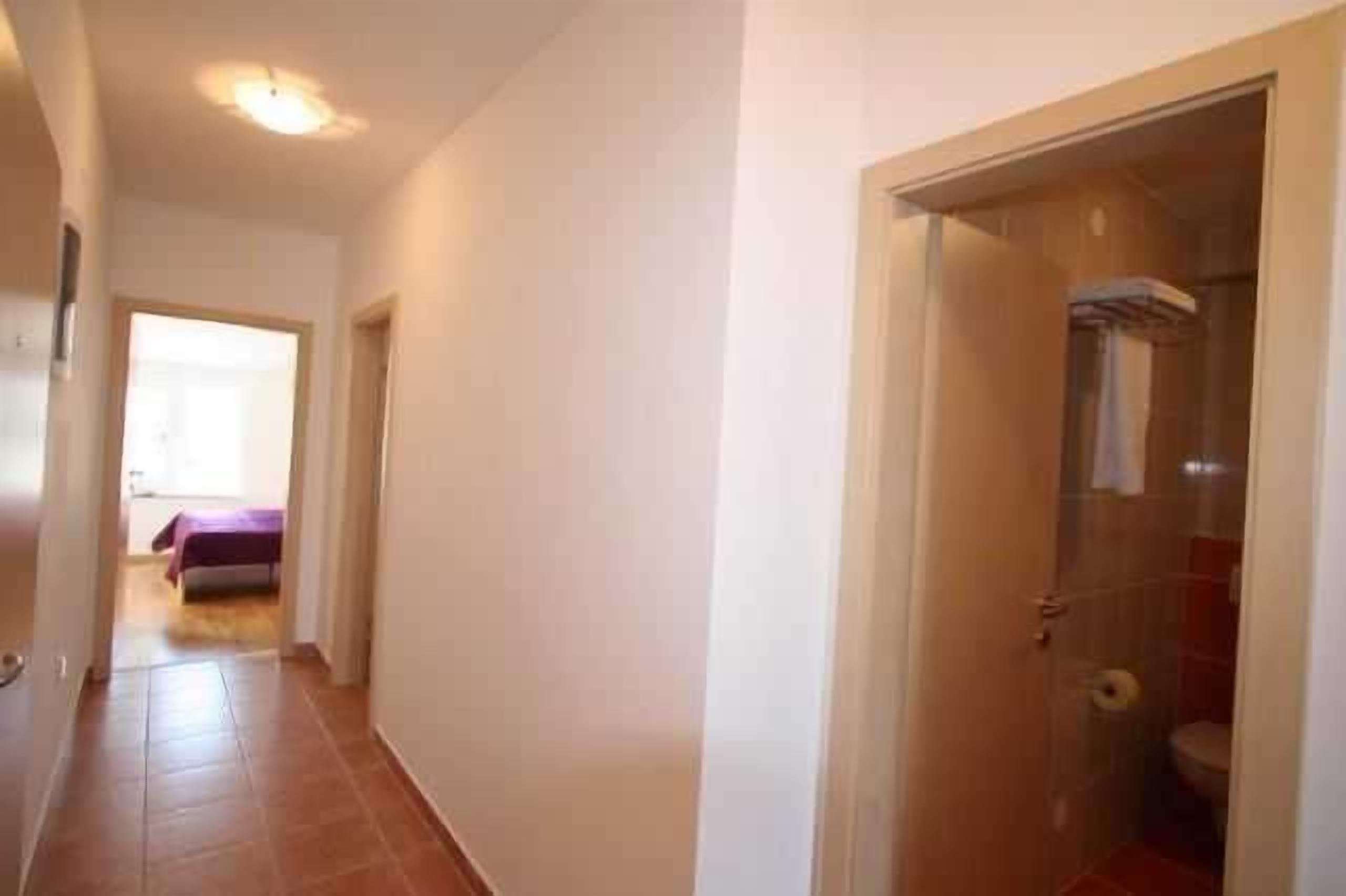 Een gang met een bed, een badkamer met een douche en een deur naar een andere kamer.