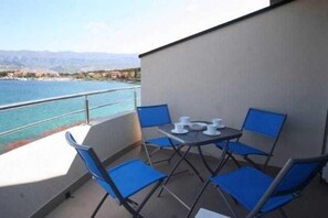 Uma varanda com mesa e cadeiras, com vista para um corpo d'água e montanhas ao longe.