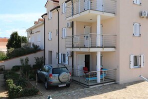 A multi-story residential building with balconies, a car parked in front, and a small garden area. - 10027-A1 · Apartment - Sonata - ( 10027-A1 ) (Silo - island Krk)