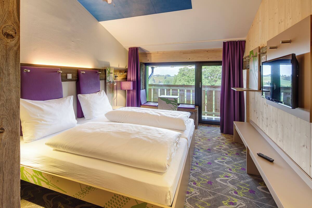 Une chambre d’hôtel avec un grand lit, une télévision, un balcon avec des rideaux et un plancher en bois.