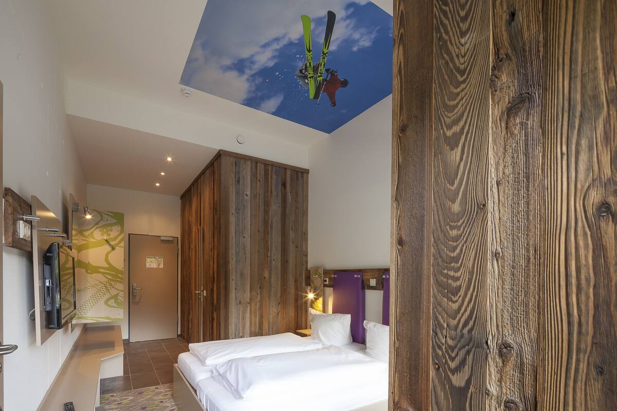 Une chambre d’hôtel avec un plafond en bois, un lit, une télévision et une salle de bain dont la porte est en bois.