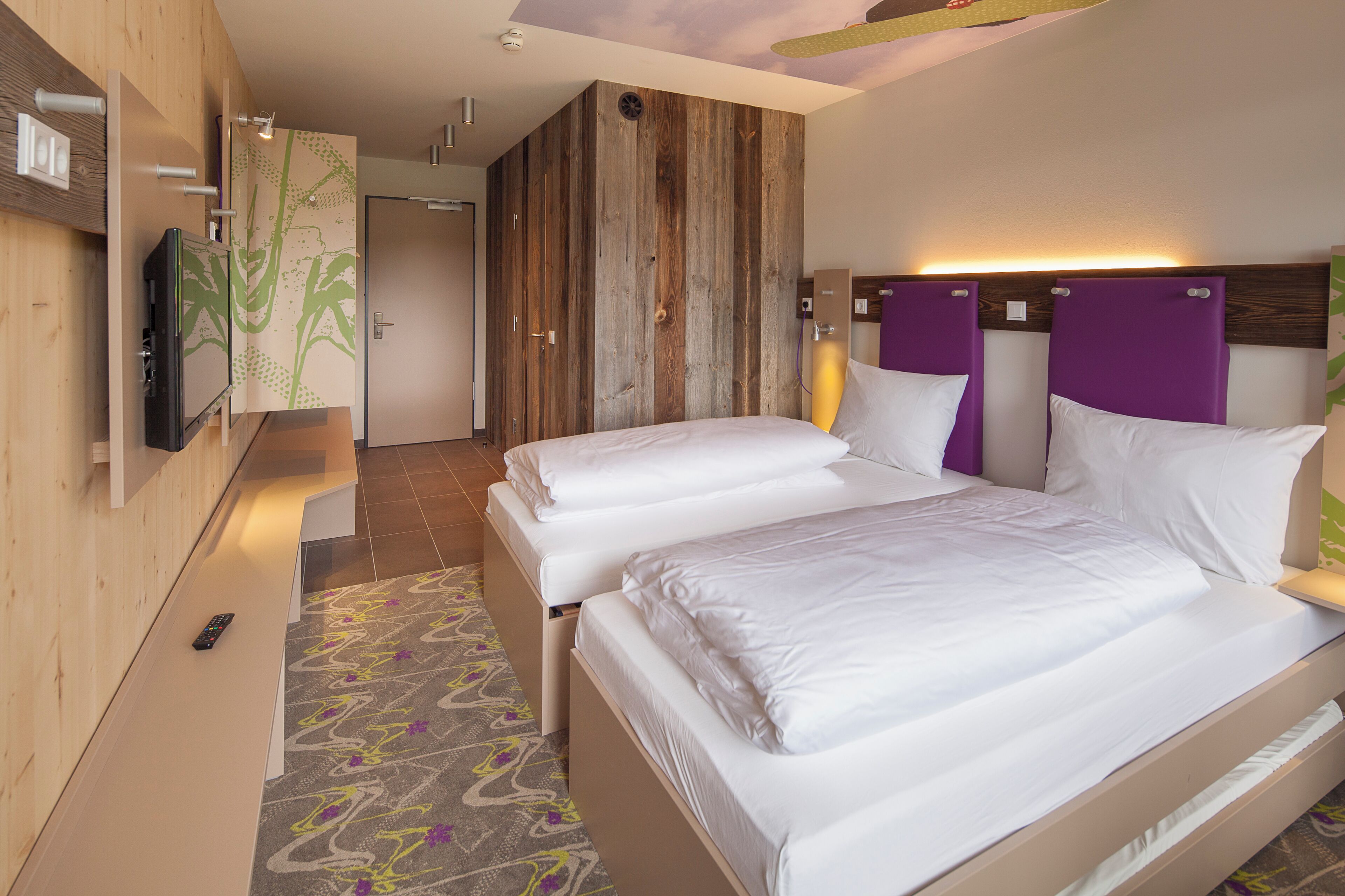 Habitación de hotel con dos camas, un televisor y una pared de acento de madera.
