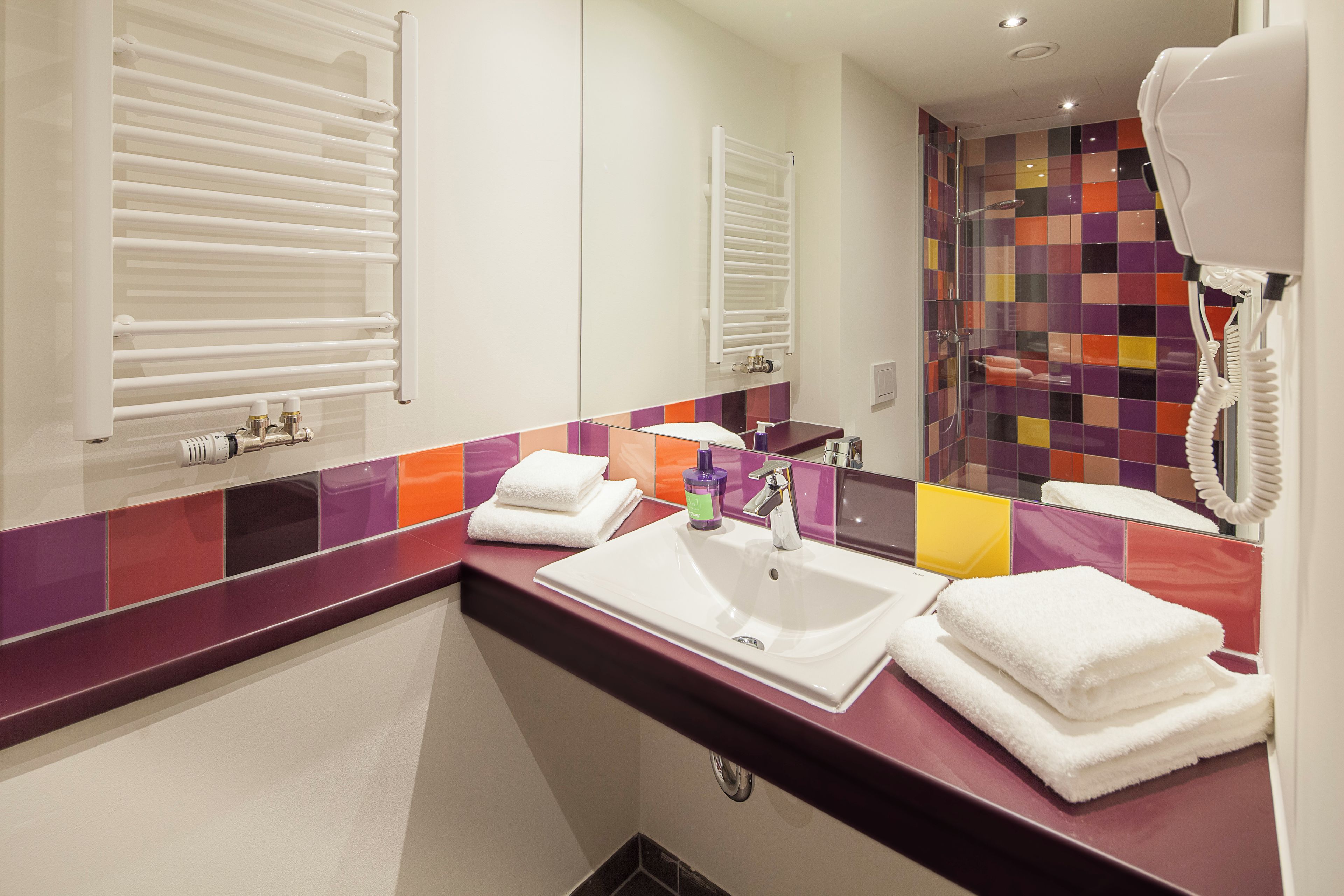Un baño moderno con lavamanos blanco, un espejo, un perchero para toallas y una zona de ducha.