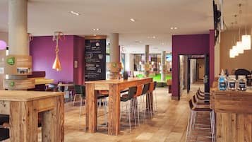A modern cafe with wooden tables and chairs, a chalkboard menu, and a green counter area.