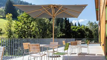 An outdoor patio with a table and chairs, a large umbrella, and a view of a green landscape.