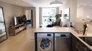 A modern kitchen with a built-in washer and dishwasher, a dining area with a round table and chairs, and a living room with a sofa and a TV. - Hydepark Executive (Randburg)