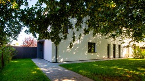 A modern building with a paved pathway leading to a door, surrounded by lush greenery and a well-maintained lawn. - Penzion Dílna (Trebon)
