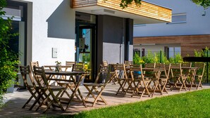 An outdoor seating area with wooden tables and chairs, a modern building with a sloped roof, and a grassy foreground. - Penzion Dílna (Trebon)
