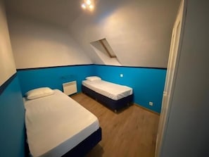 A small, single-room bedroom with two beds, a sloped ceiling, and blue walls. - Zeezicht 703 (Nieuwpoort)