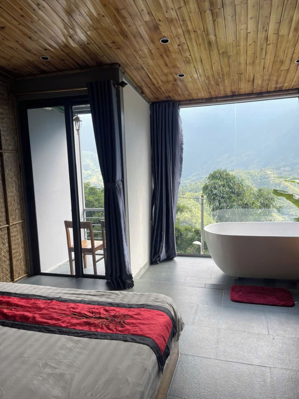 A bedroom with a large bed, a bathtub, and a view of a mountainous landscape.