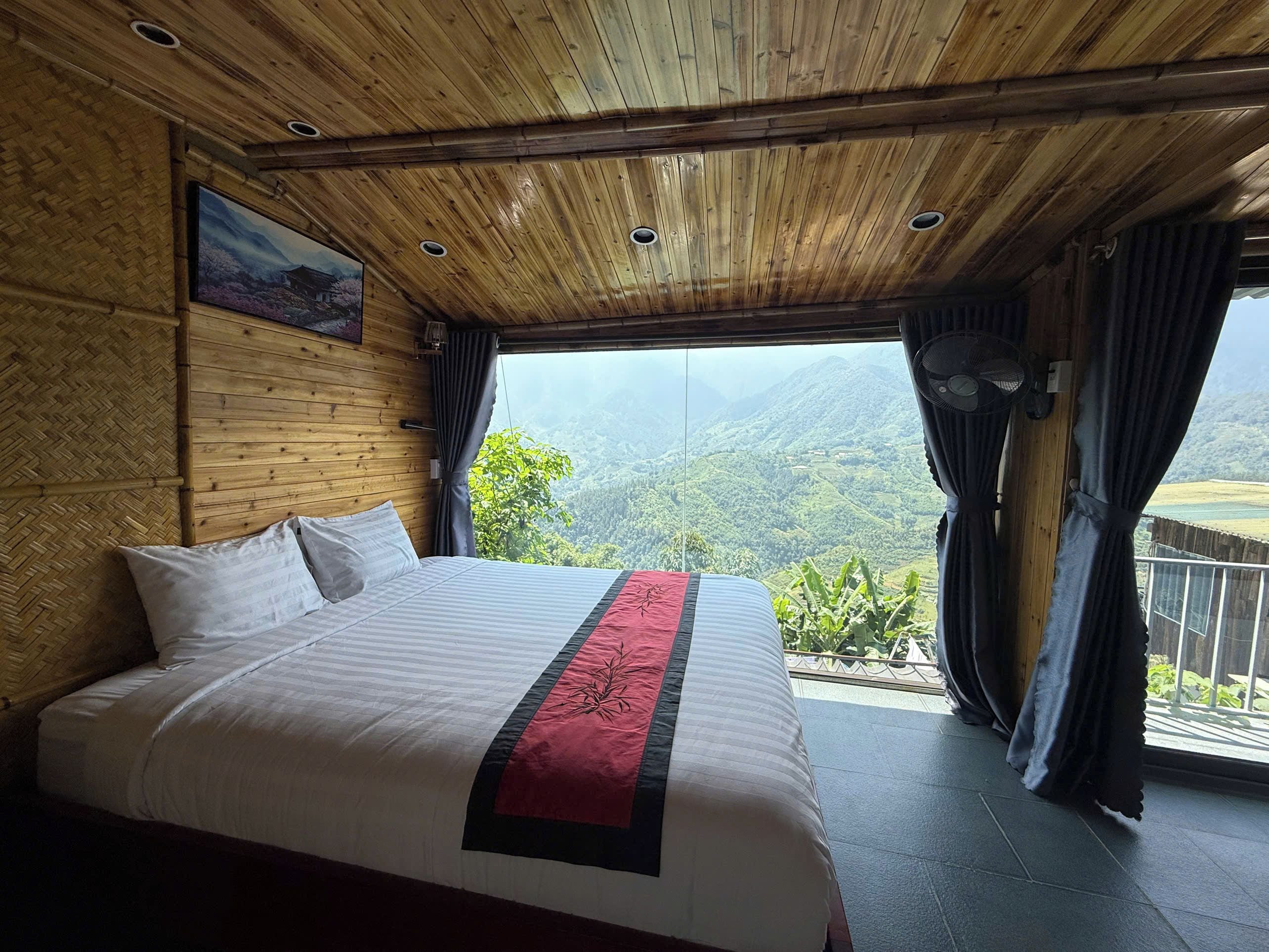 A bedroom with a large bed, wooden ceiling, and a view of a mountainous landscape.