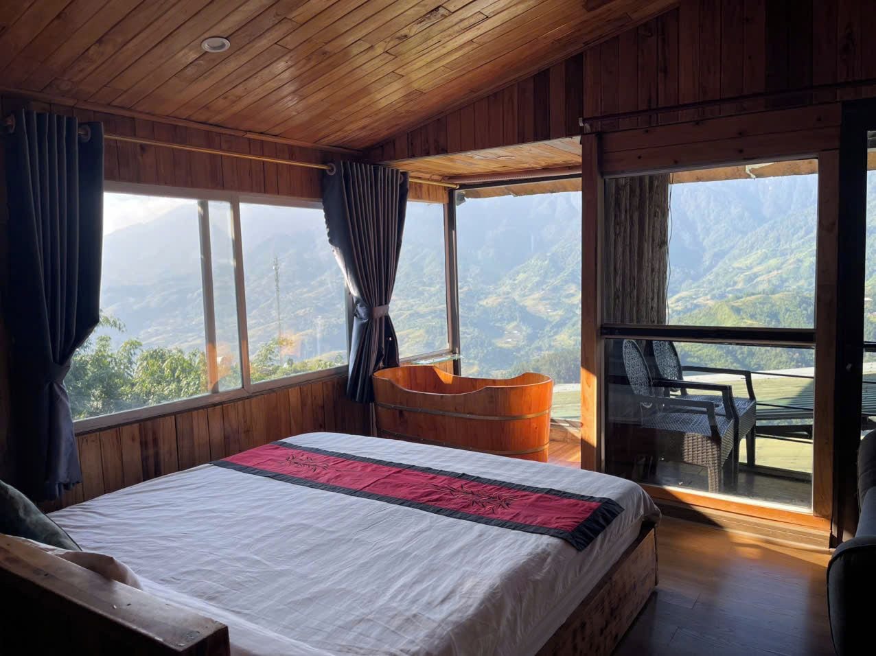A bedroom with a large bed, a wooden ceiling, and a view of mountains through a large window.