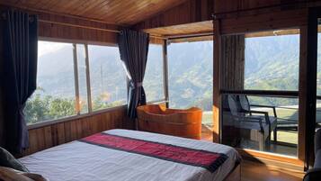 A bedroom with a large bed, a wooden ceiling, and a view of mountains through a large window.