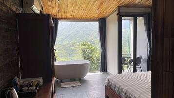 A bedroom with a large bathtub, a bed, and a view of a mountainous landscape.