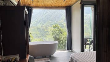 Un dormitorio con una bañera grande, una cama y vistas a un paisaje montañoso.
