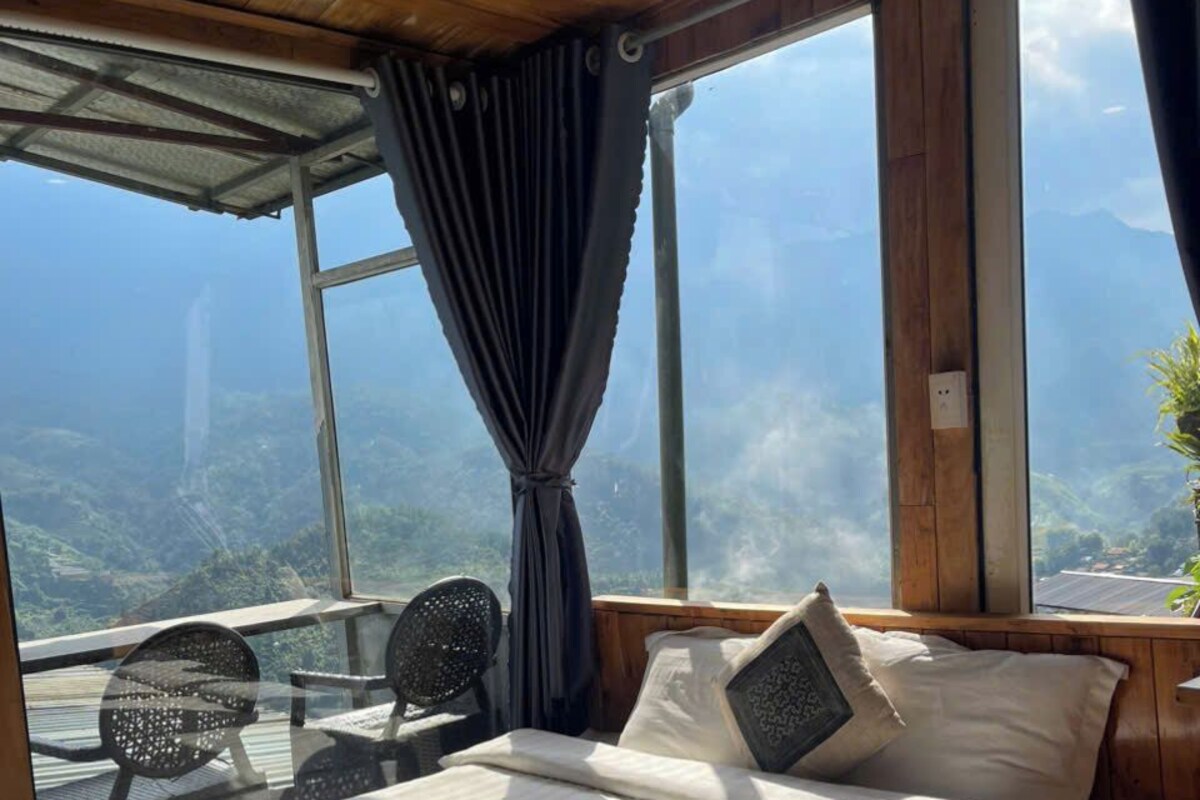 Een slaapkamer met een groot bed, een raam met gordijnen en uitzicht op een bergachtig landschap.