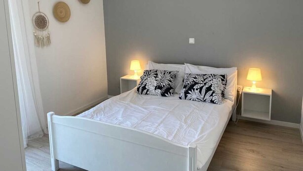 Una cama con ropa de cama blanca, dos lámparas de noche y una pared decorada con tres piezas de arte circular.