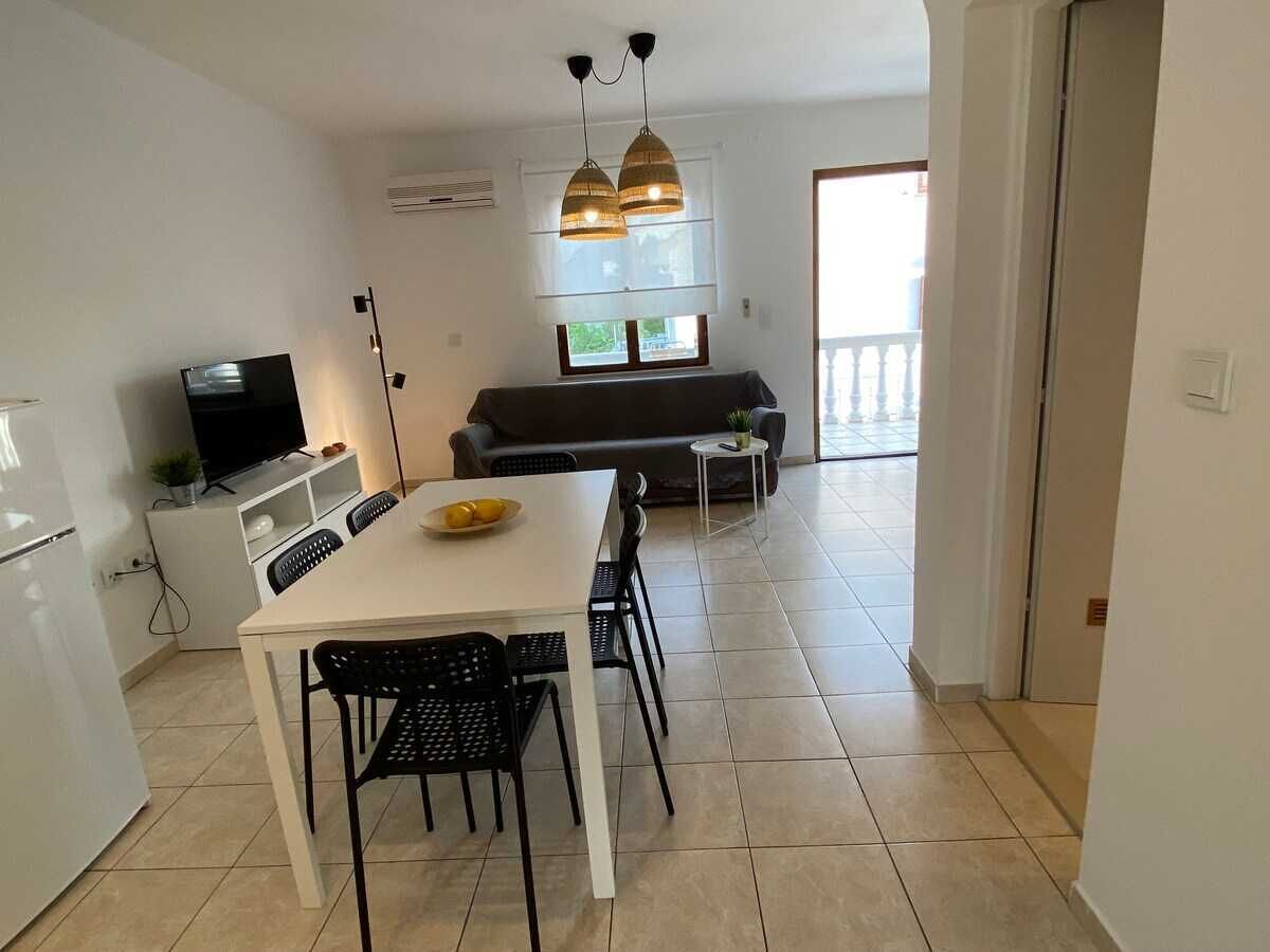 A modern kitchen with a dining table, chairs, a TV, and a sofa in the background.