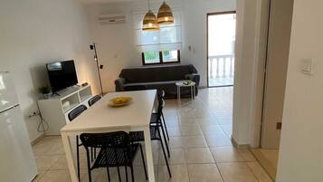 A modern kitchen with a dining table, chairs, a TV, and a sofa in the background.